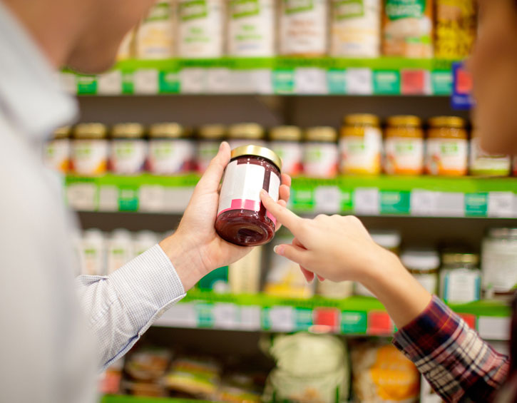 A man and a woman inspect the nutrition label of a jarred food.