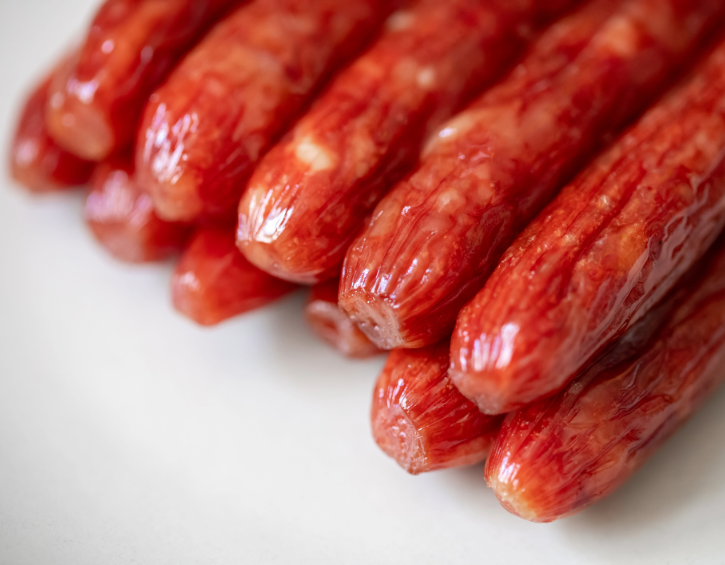 Glossy red meat sticks stacked on a white surface, showcasing texture and flavor.